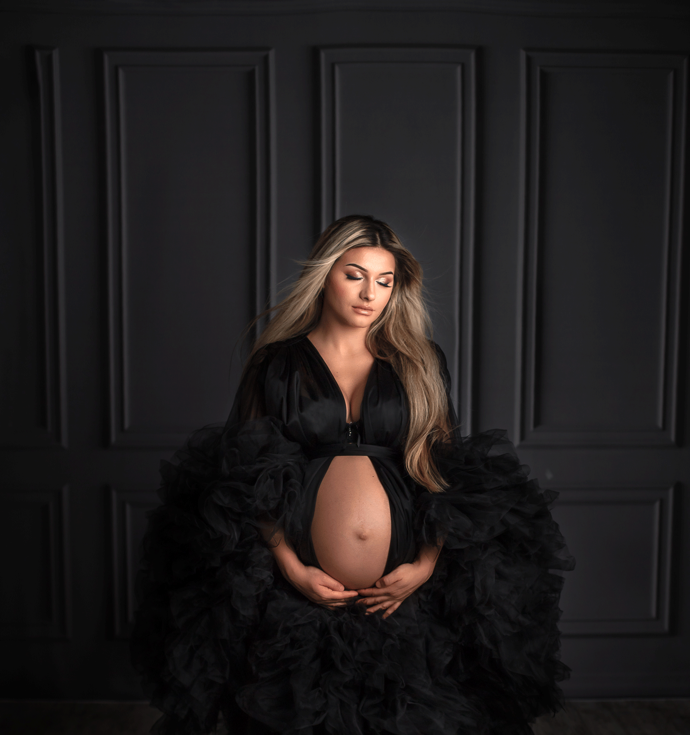 Pregnant woman cradling baby bump, illustrating when to book a maternity session in a fine art photography setting by Sonia Gourlie.