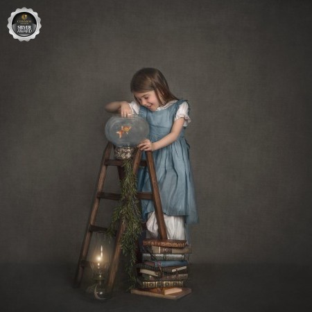 Girl playing with her fish , standing on a ladder wearing a soft blue dress , captured the photography studio in Ottawa Ontario 