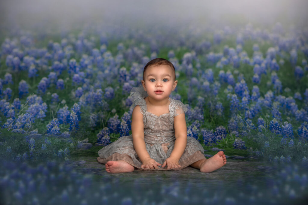 Baby girl sitting in a dreamy bluebonnet field, wearing an elegant lace dress during a Spring Mini Portrait Session 2025