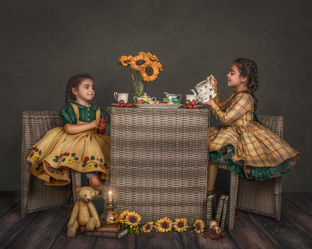 Two young sisters enjoying a whimsical tea party surrounded by sunflowers in a styled studio photography session in Ottawa