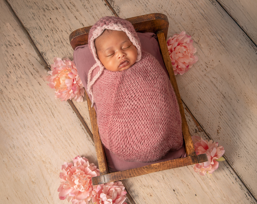 Close-up of a sleeping newborn girl in a basket and wooden bed, styled with soft pink wraps and natural textures, Ottawa.