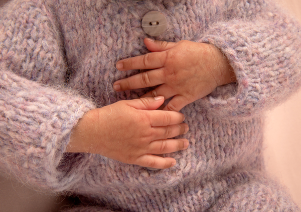 Close-up of newborn girl’s tiny hands in lavender knit outfit with soft pink details, Ottawa newborn session.