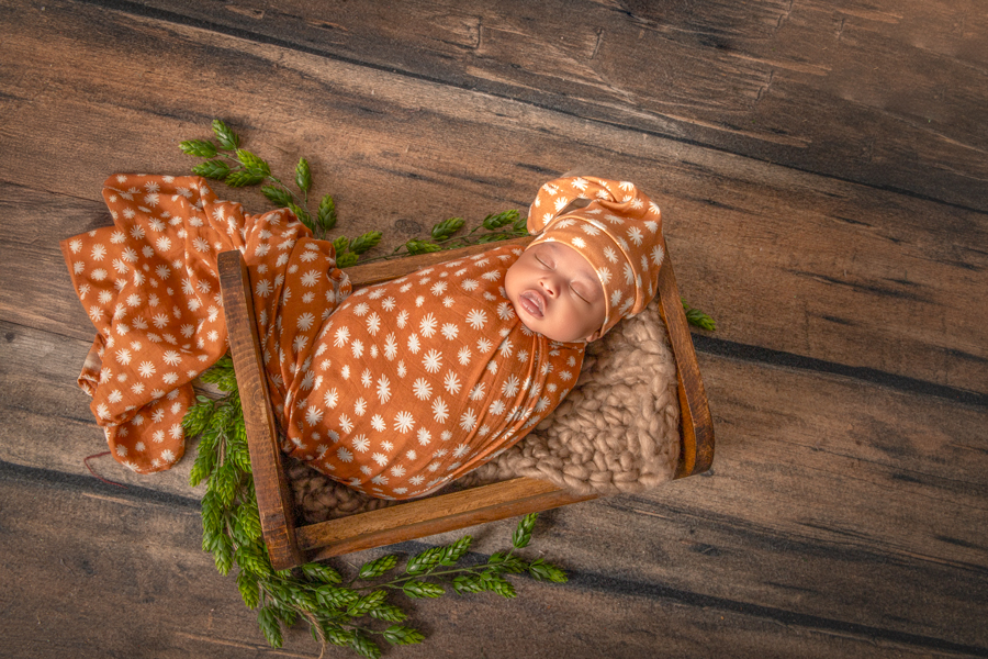 Close-up of newborn girl wrapped in a family’s cultural wrap with brown and yellow hints, complementing soft pink and lavender tones, Ottawa newborn session.