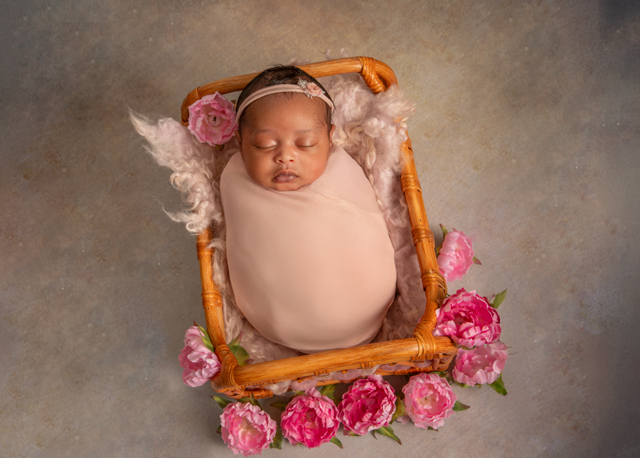 Newborn baby girl sleeping peacefully in a basket with soft pink and lavender wraps, styled by Ottawa newborn photographer Sonia Gourlie
