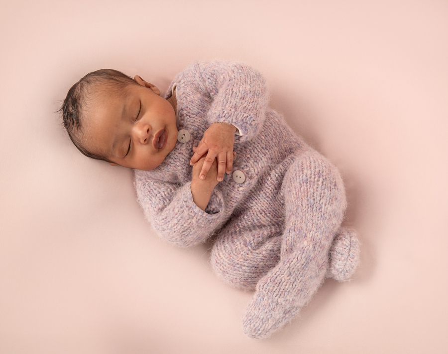 Sleeping newborn girl in lavender knit outfit with soft pink hints, traditional pose for Ottawa newborn photography.